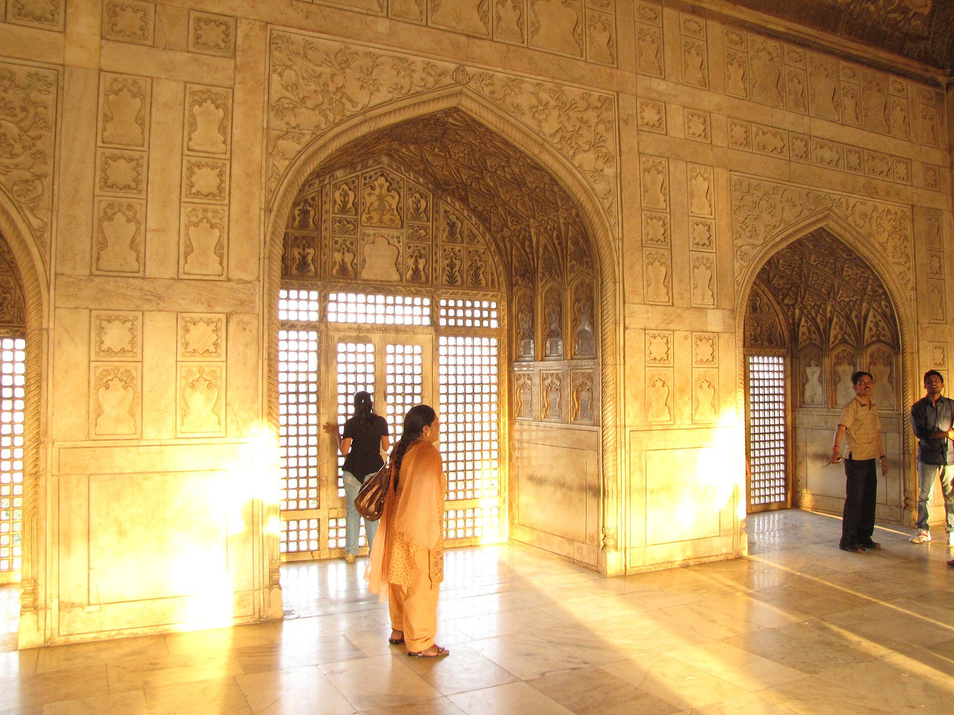 A sunlit hall in Agra Fort, visitors small against the light from the jali