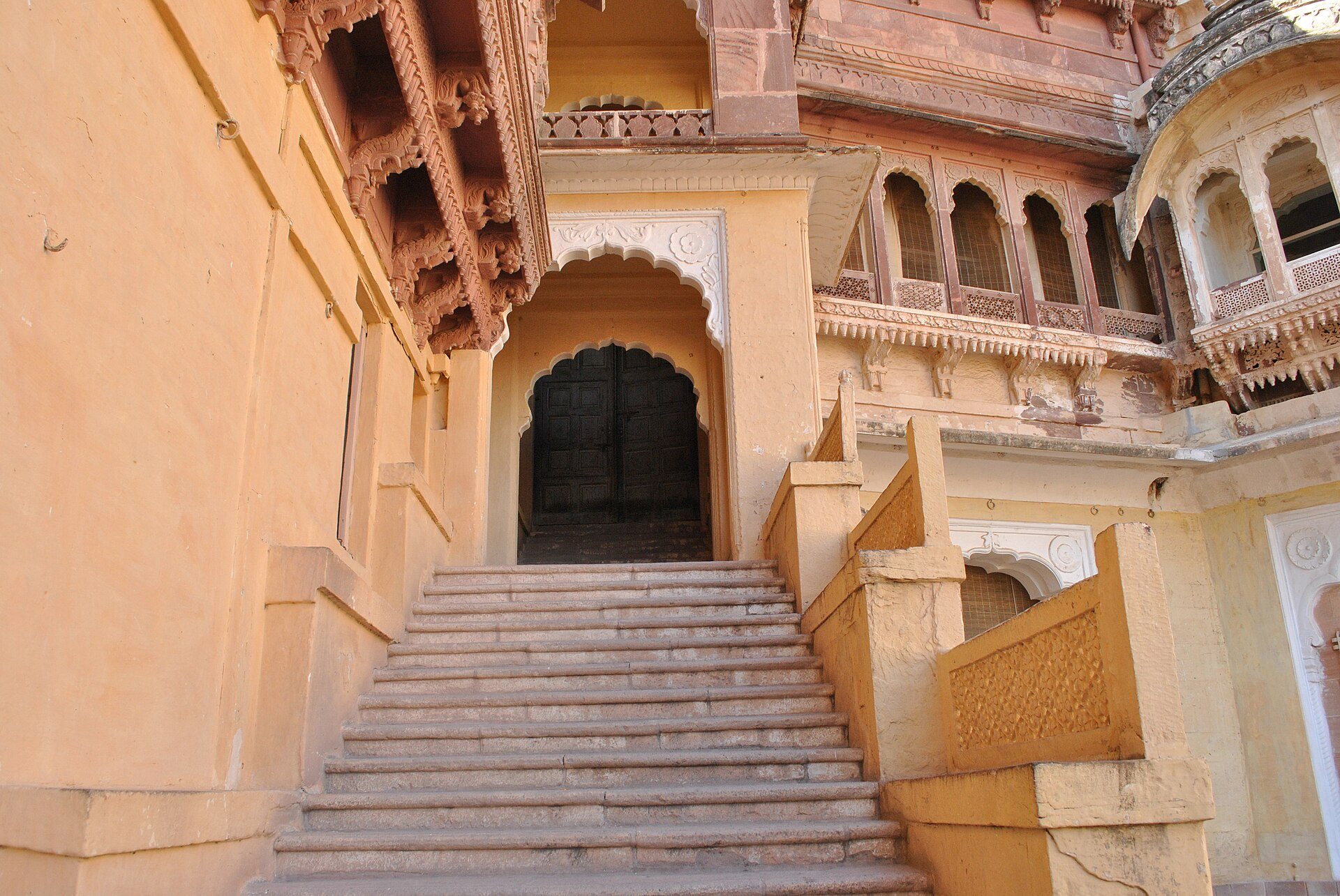A flight of stone steps inside Mehrangarh in Jodhpur, rising to a closed door between carved sandstone walls, with no handrail on either side