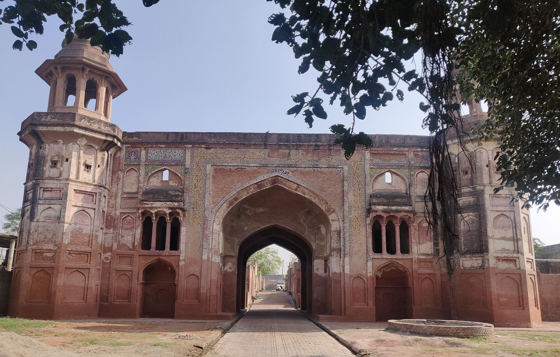 The Lahore gateway of Sarai Amanat Khan on the old Delhi-Lahore road, its glazed-tile calligraphy bands still legible above the arch, with the path running through into the inhabited sarai beyond