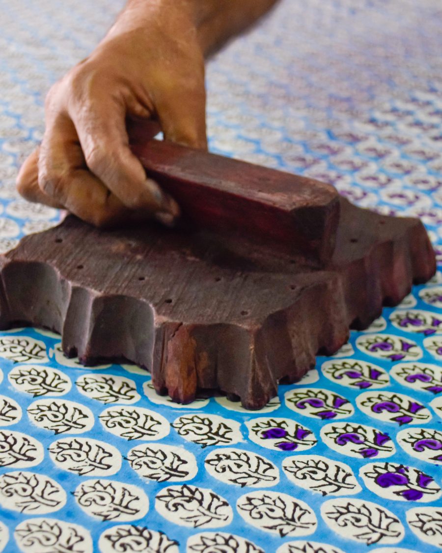A block-printer's hand pressing a carved wooden block onto indigo-patterned cloth, Rajasthan